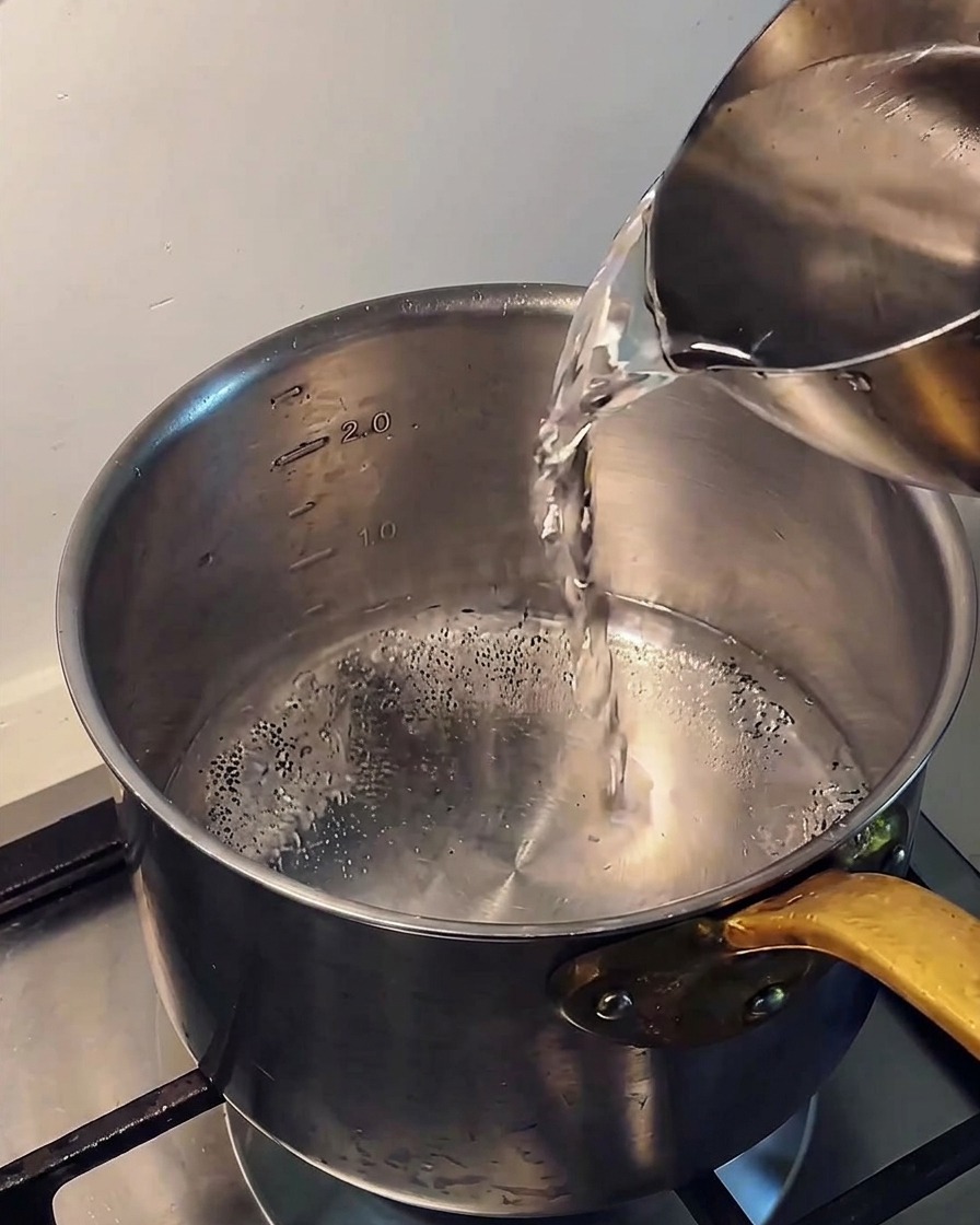金属製のピッチャーからステンレス鍋に冷水を注いでいる様子。
