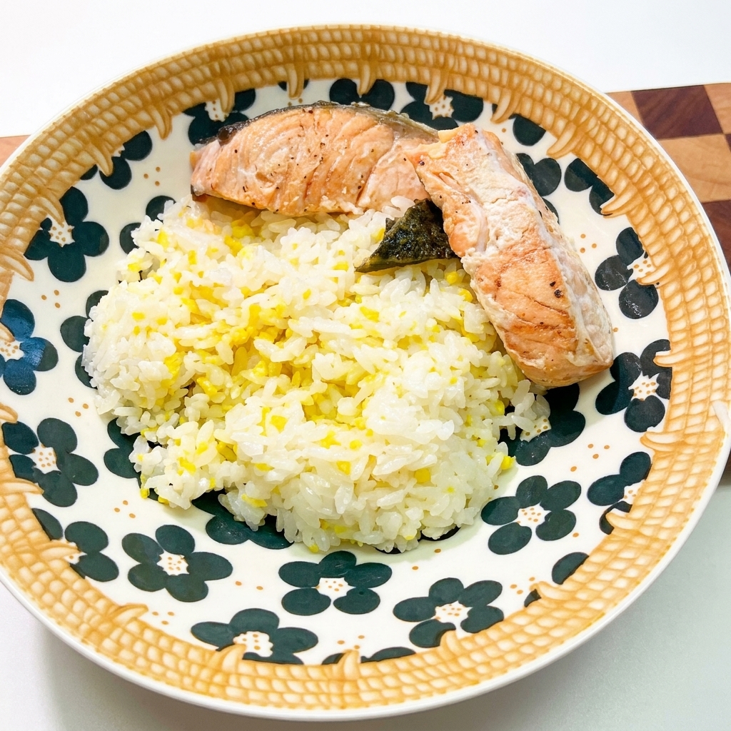 美しい模様の陶器の丼に盛られた白いご飯の上に、調理されたサーモン2切れと海苔が乗っている様子。