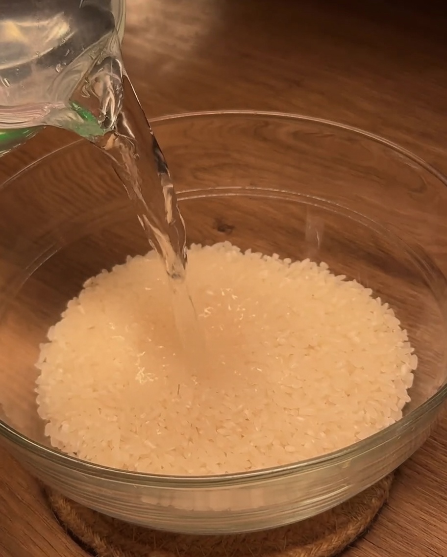 米が入ったガラスボウルに計量カップで水を注いでいる様子。