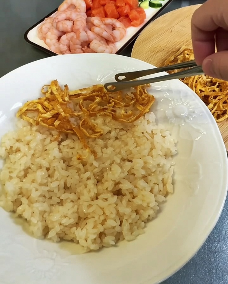 大きな白い皿に酢飯を広げ、錦糸卵と海鮮具材を並べている様子。