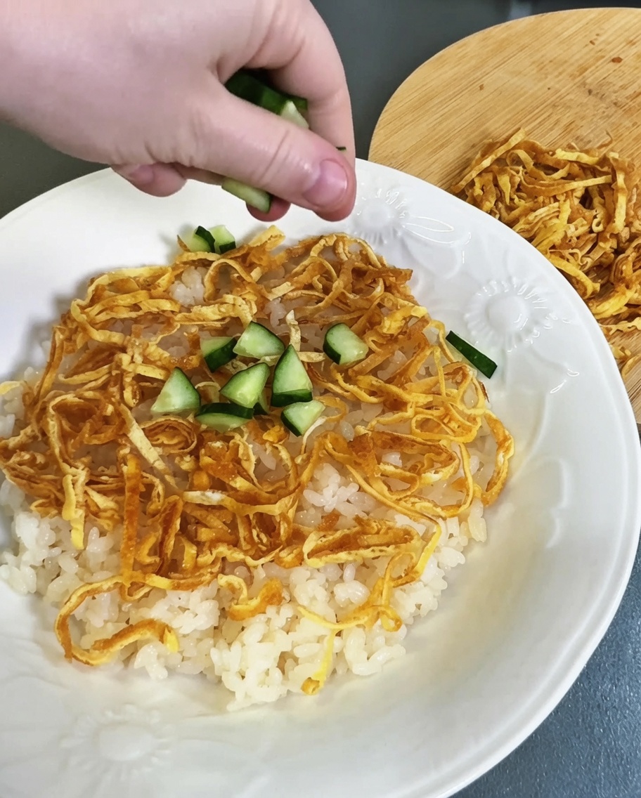 用意した酢飯と錦糸卵の上に、角切りにしたきゅうりを散らしている様子。