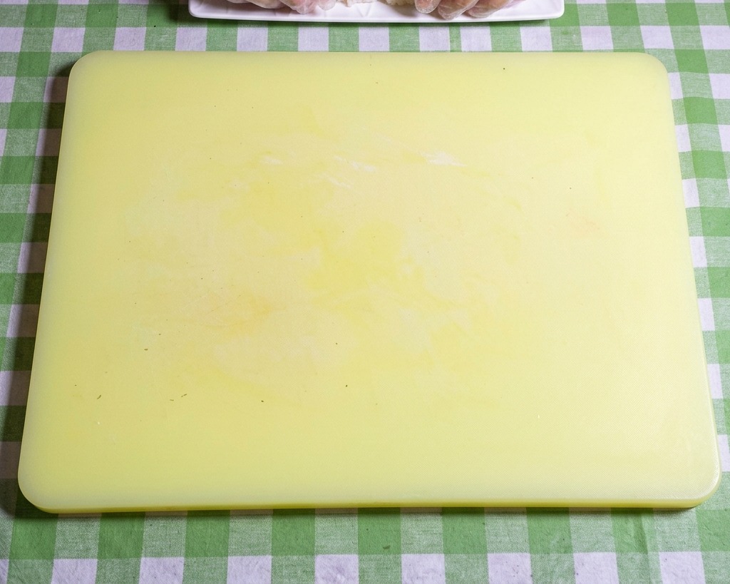 黄色いまな板の上で、手袋をした手で酢飯を俵型に整えているクローズアップ画像。