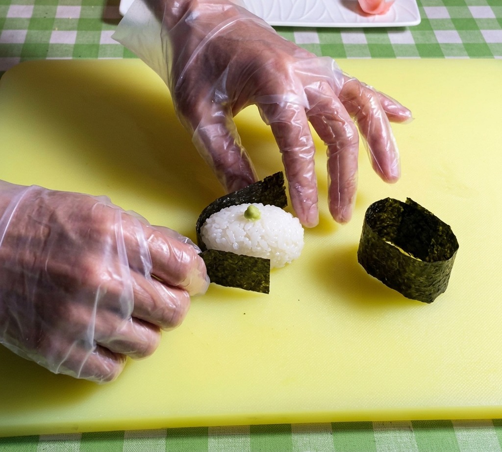 俵型の酢飯の周りに、細長い海苔を巻きつけている様子。
