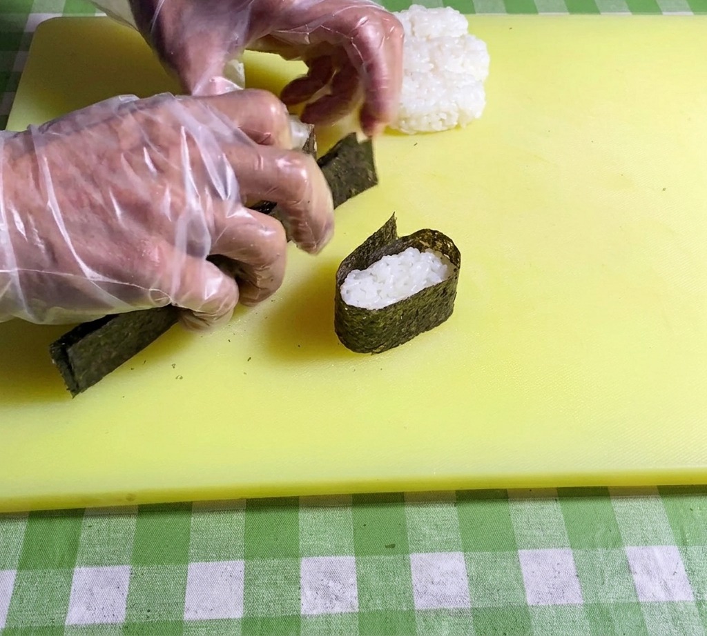 海苔の端を酢飯に押し当てて、しっかりと密着させている様子。