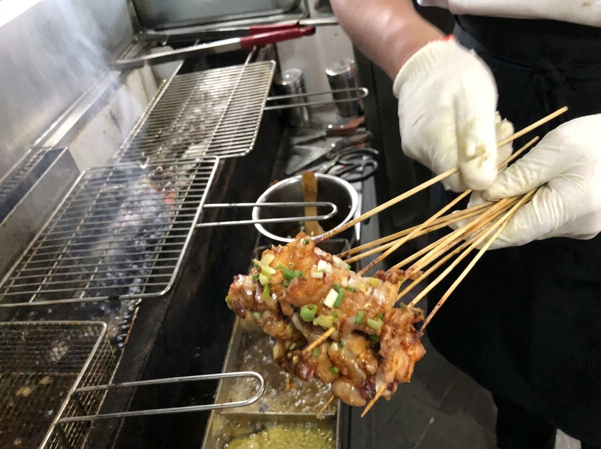 炭火焼きのグリルで焼いている豚バラ串に、刷毛でタレを塗っている様子。
