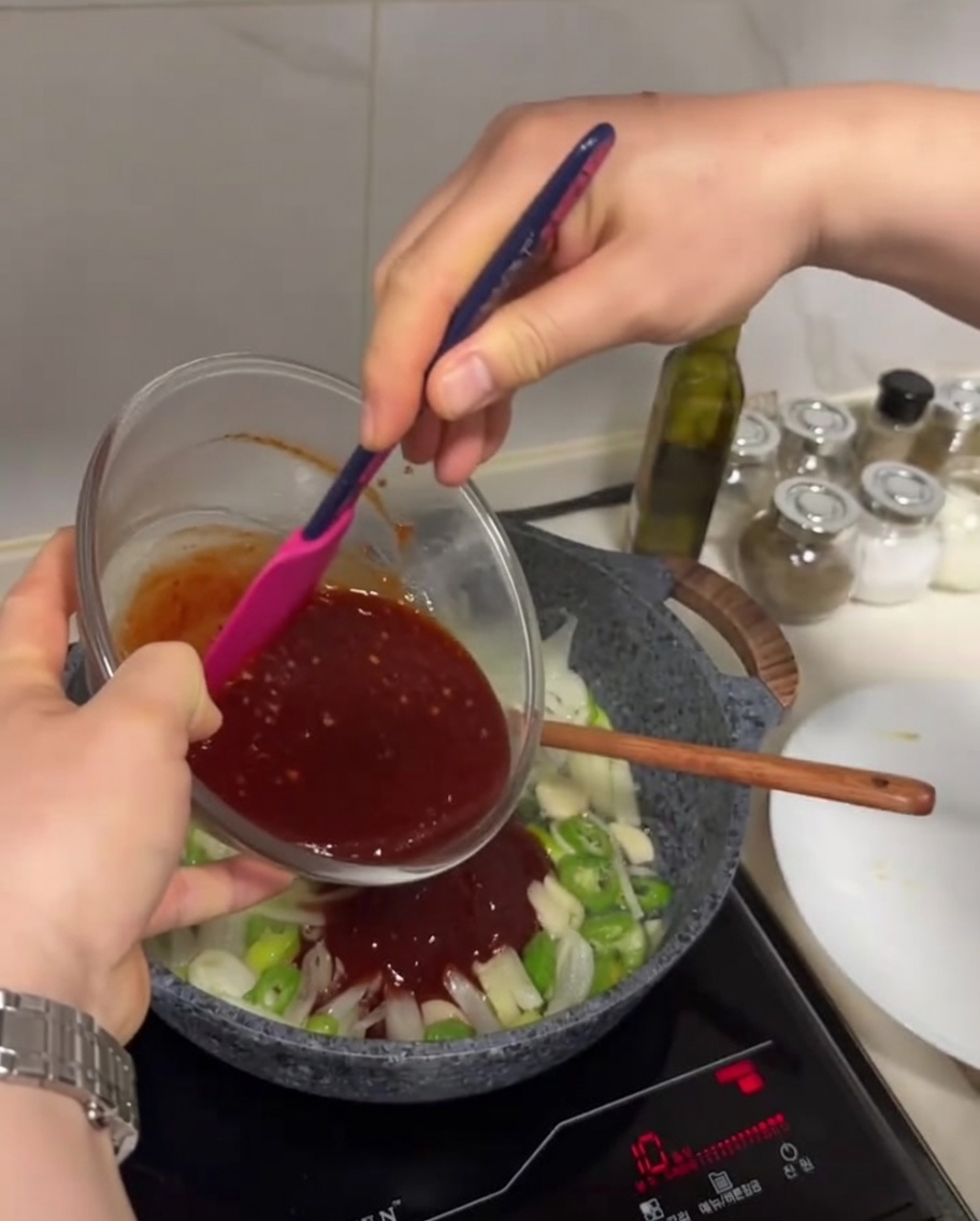 炒めた野菜の中に赤いソースを流し込んでいる様子。