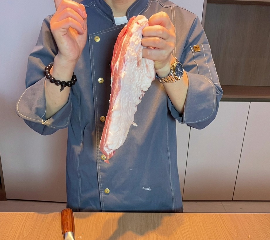 まな板の上で生の豚バラ肉を厚めに切り分けている様子。