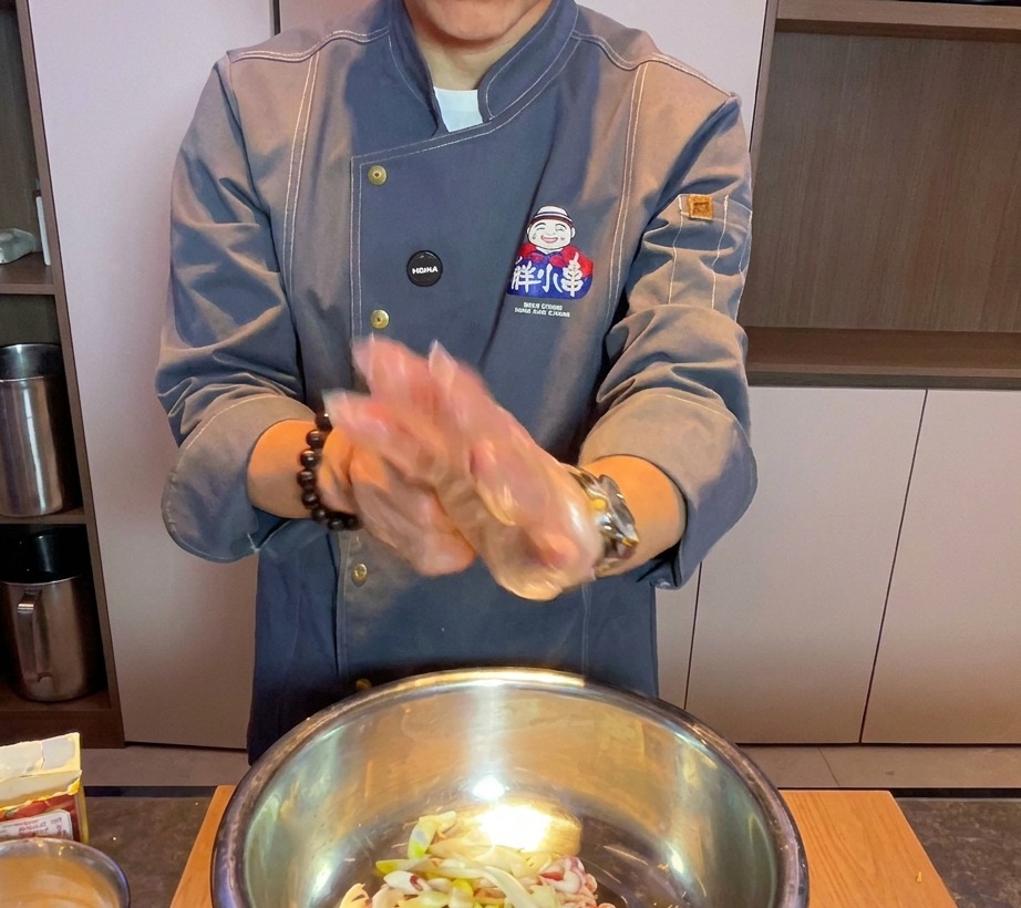 手袋をした手で、ボウルの中の豚バラ肉を揉み込んでいる様子。