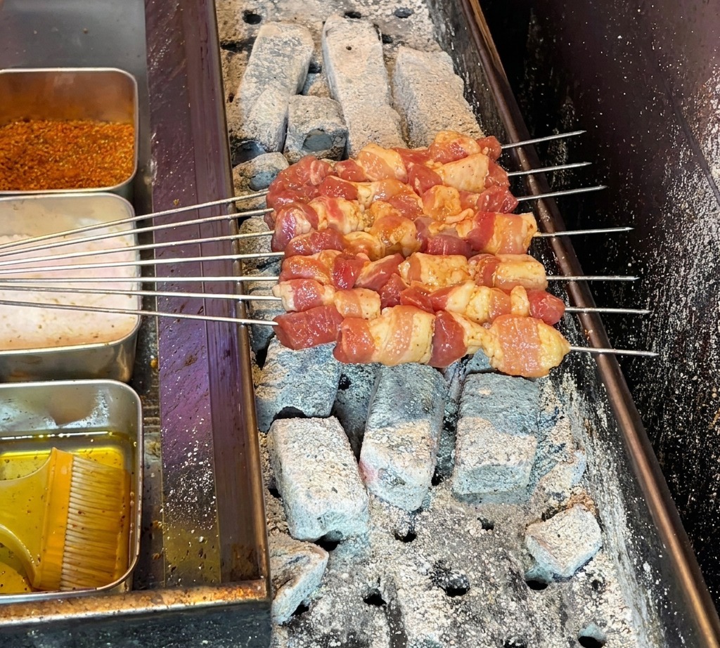 熱い炭火グリルに豚バラ肉の串を並べて焼いている様子。