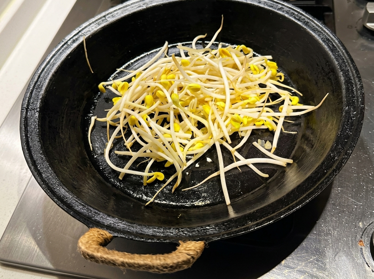 温めた黒いフライパンに、洗った豆もやしを広げている様子。