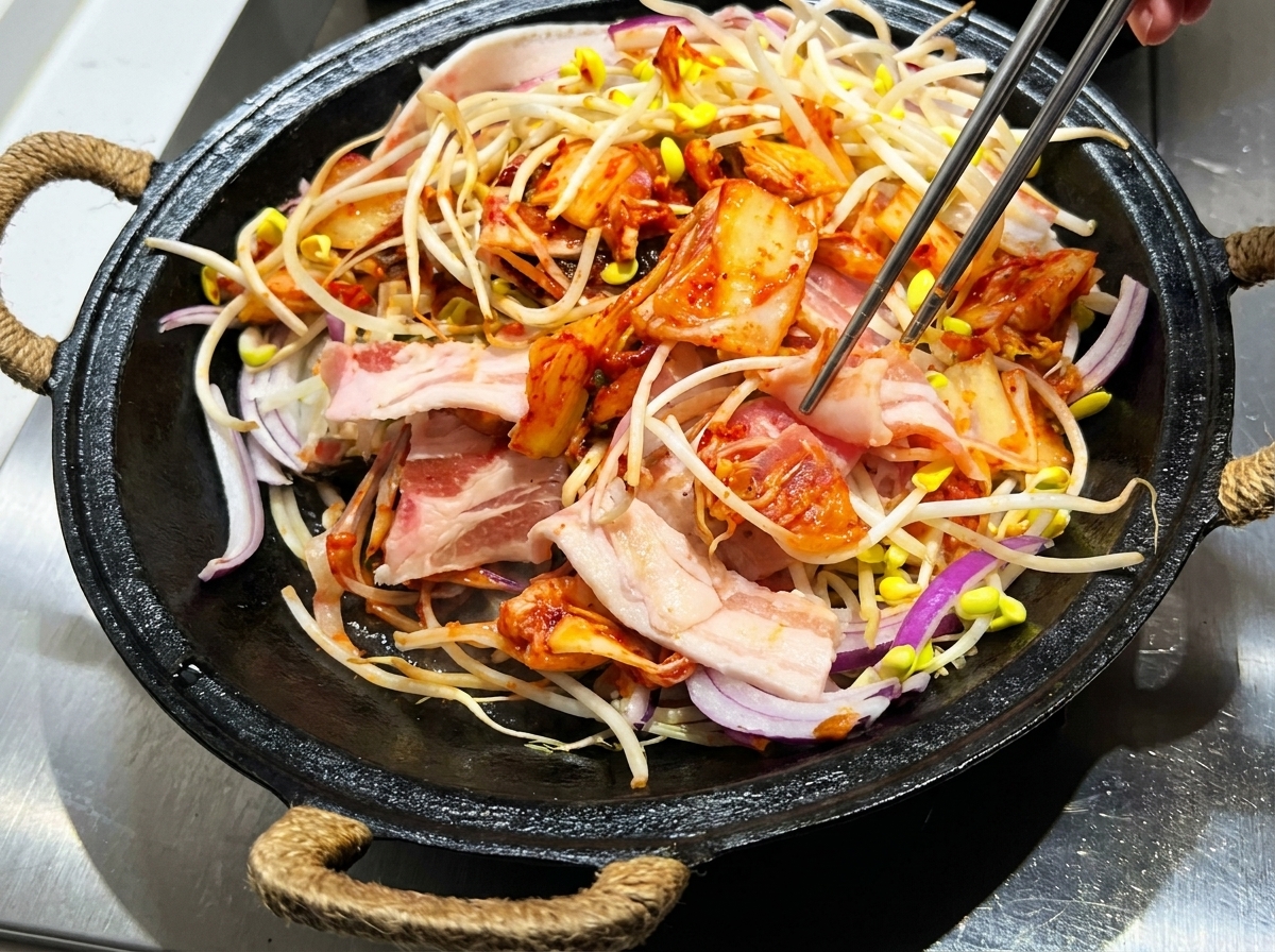 トングで肉、もやし、キムチ、タレを混ぜ合わせている様子。