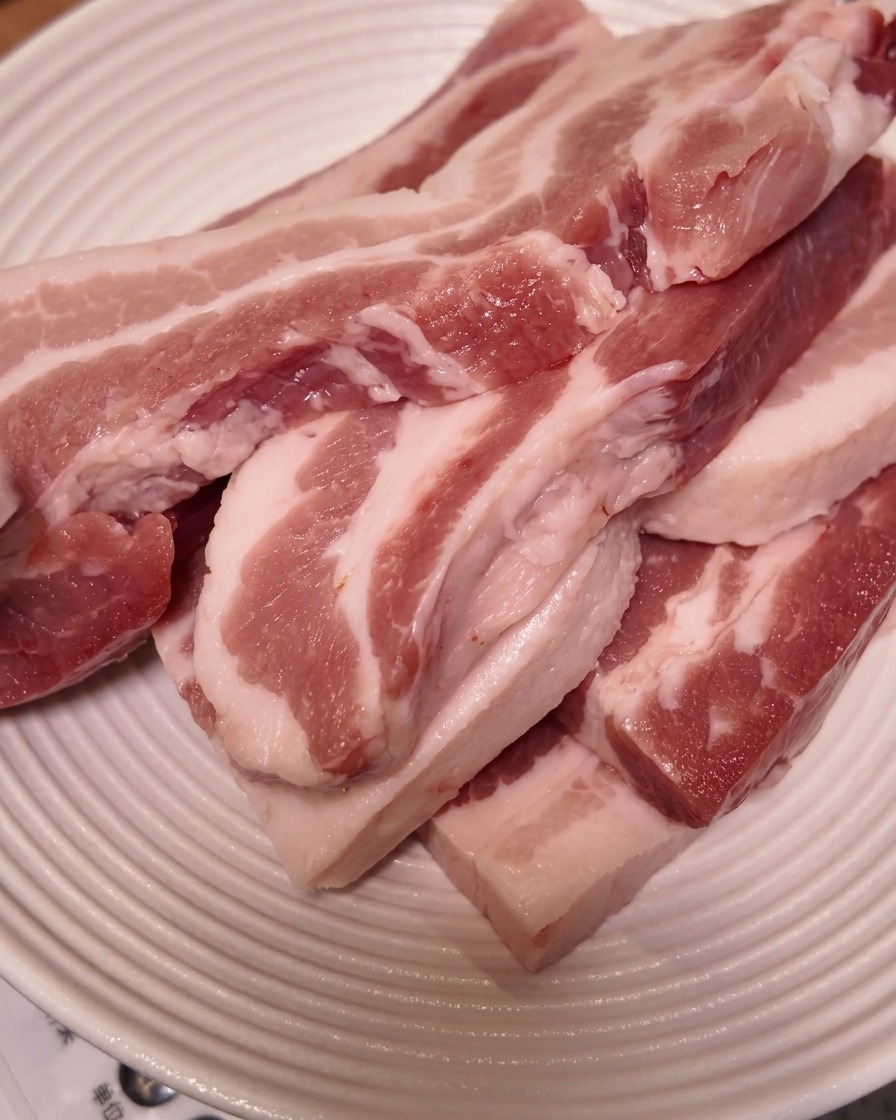 白い溝付きの皿に重ねられた厚切りの生の豚バラ肉。