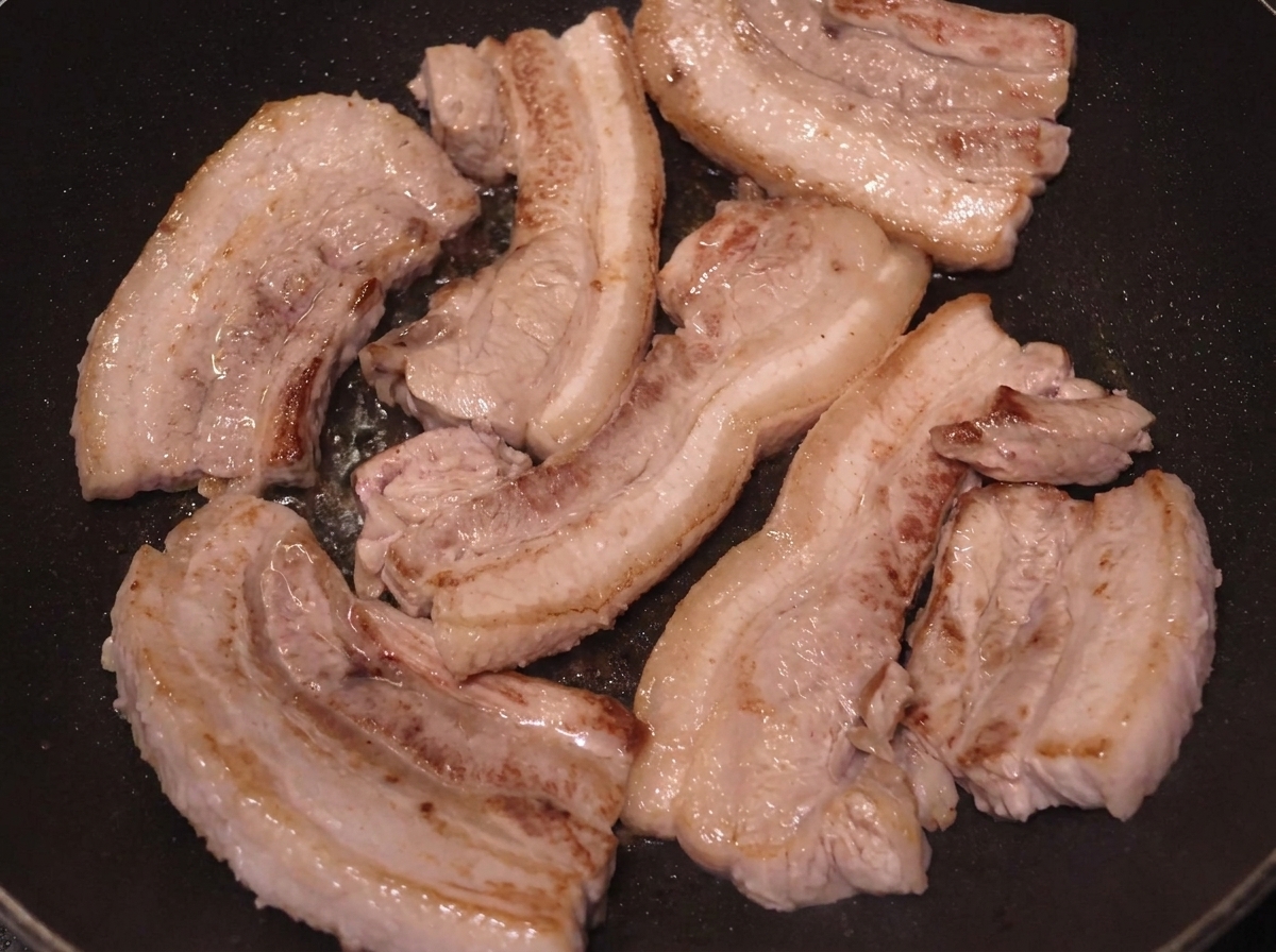 表面にこんがりと焼き色がつくまで焼かれている豚バラ肉。
