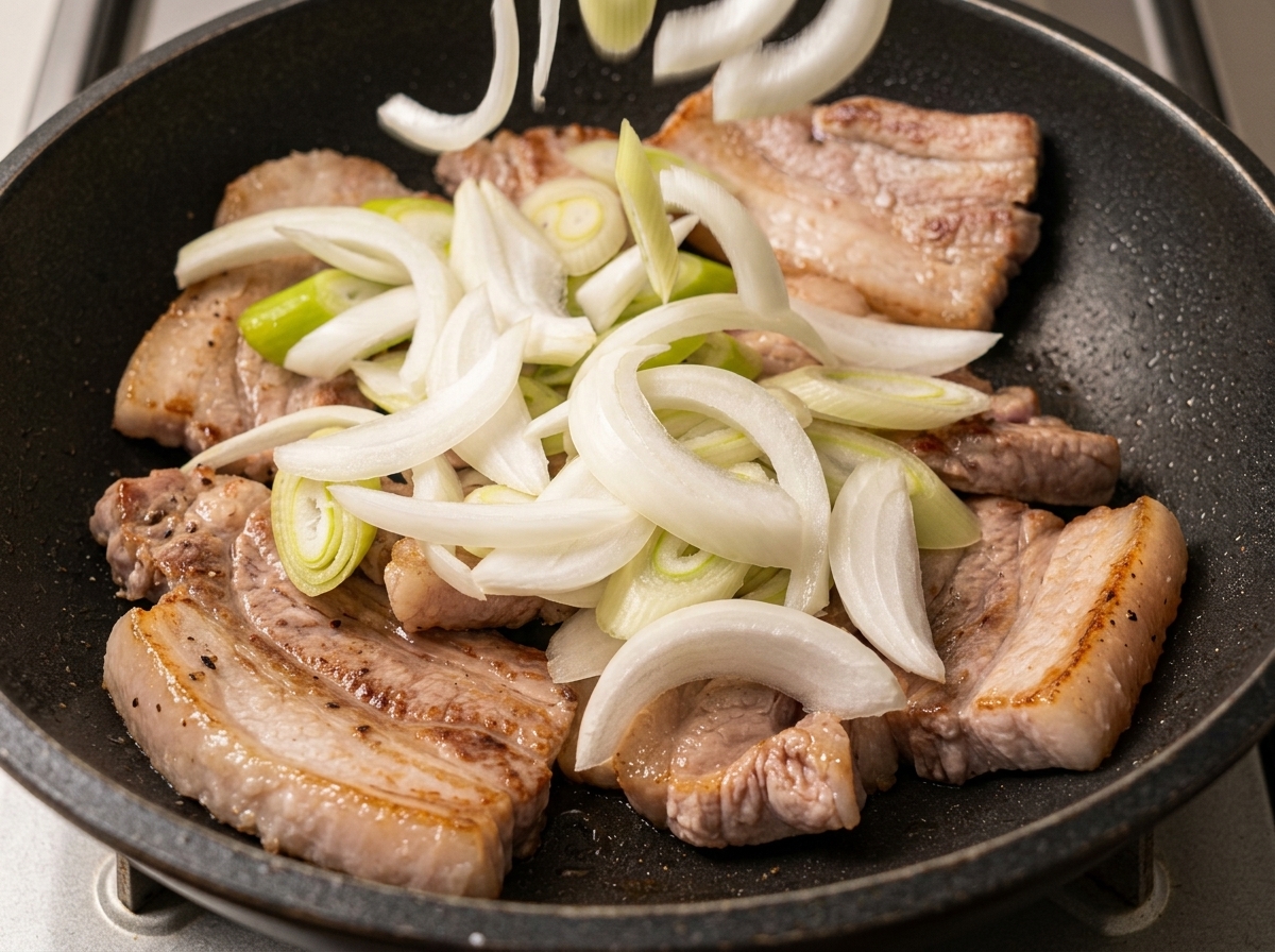 焼き色がついた豚バラ肉の上に散らされたスライス玉ねぎと長ねぎ。