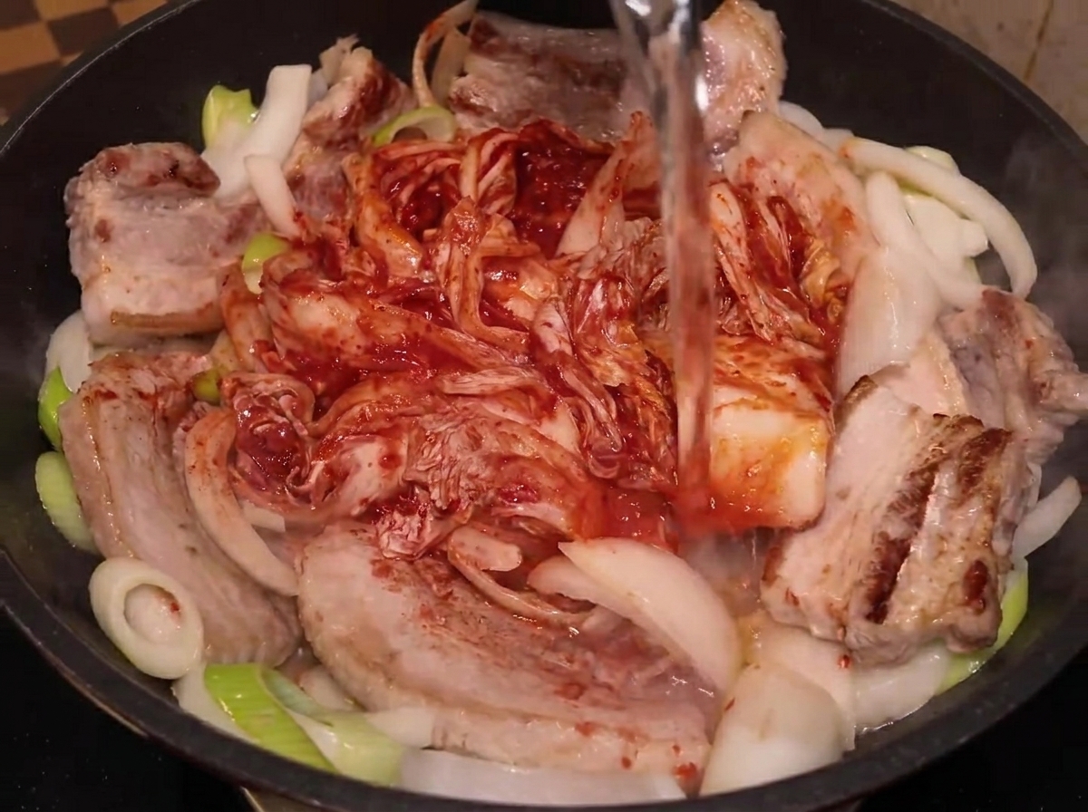 豚肉、野菜、キムチが入った鍋に水が注がれている様子。