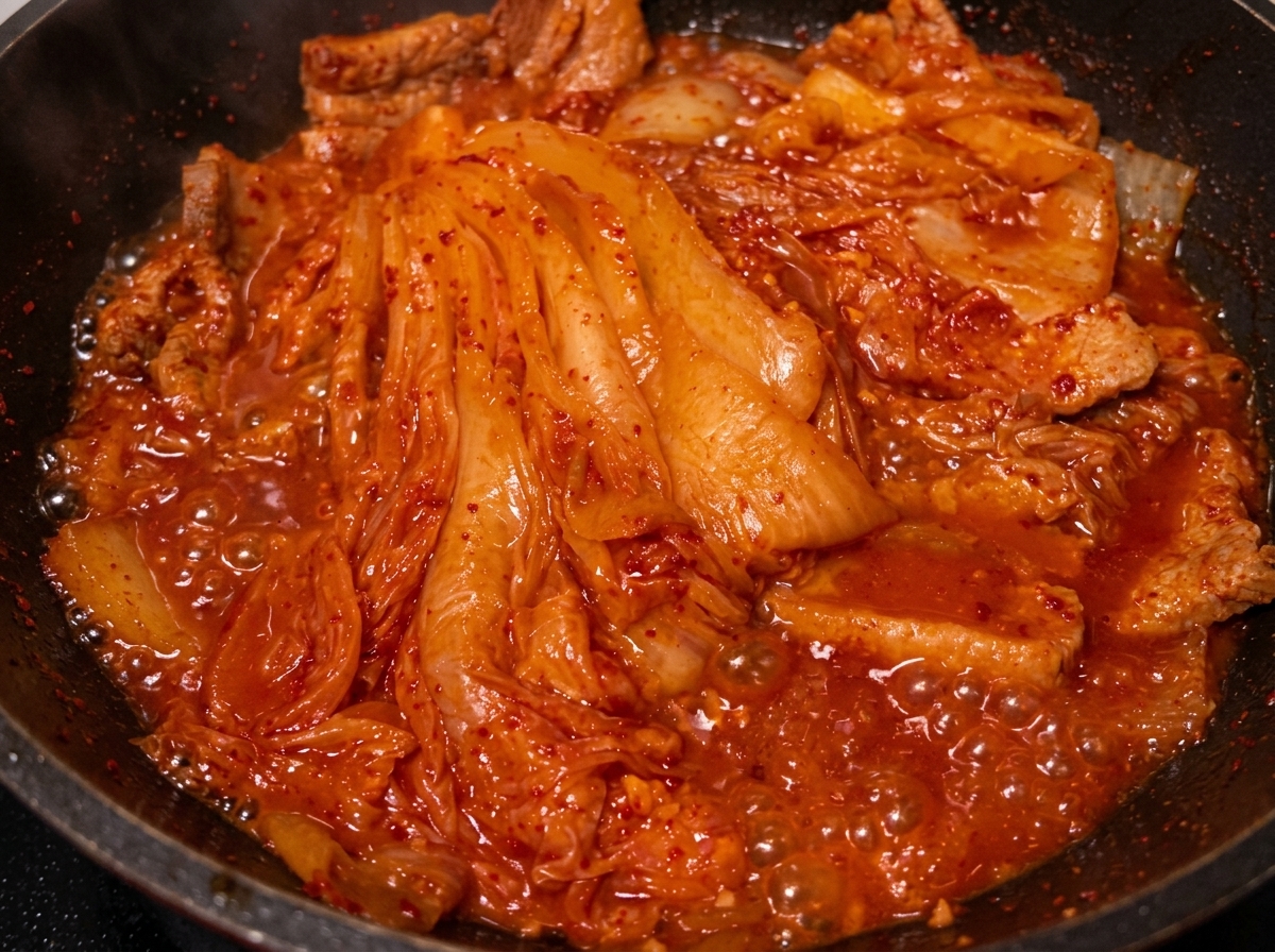煮込んだ豚肉とキムチが入った鍋に、スプーンから油を回しかける様子。