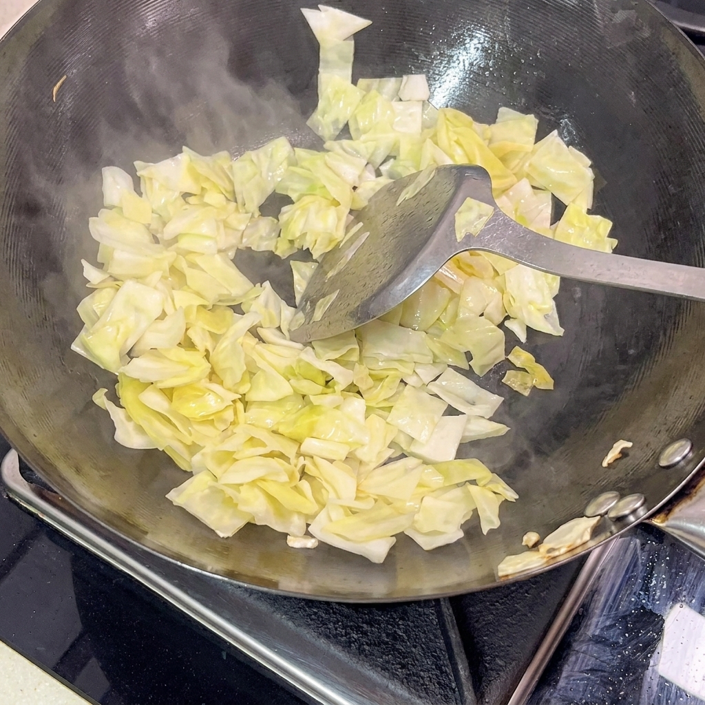中華鍋の中で高菜を炒め、湯気が上がっている様子。