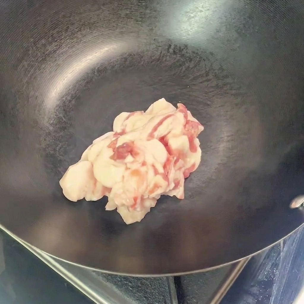 空になった熱い中華鍋に、豚バラ肉を入れる様子。
