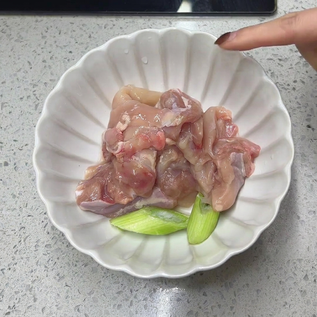白いボウルに入った生の鶏もも肉と青ネギのざく切り。