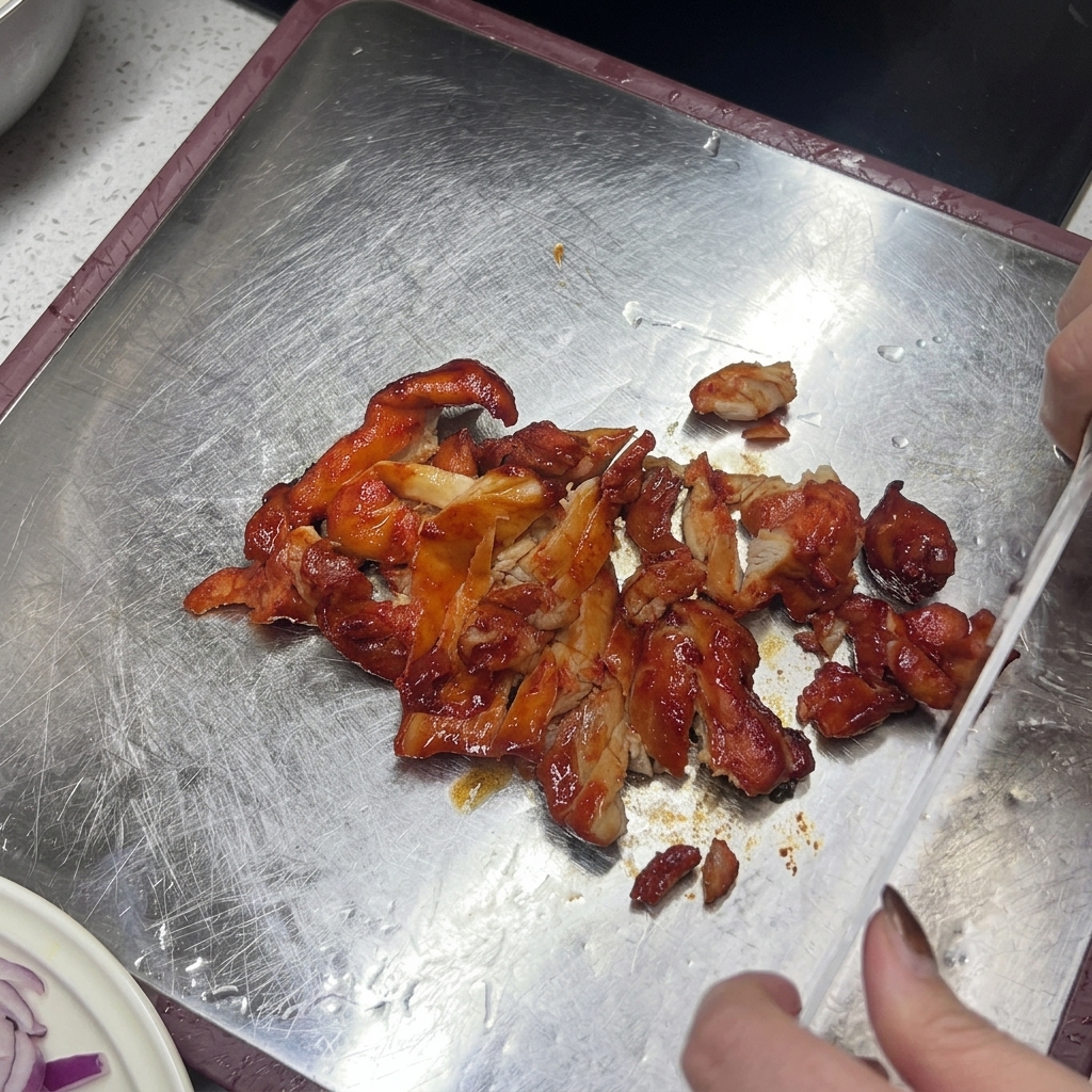 金属製のまな板の上で、赤茶色に焼けたチキンを包丁で切っている様子。