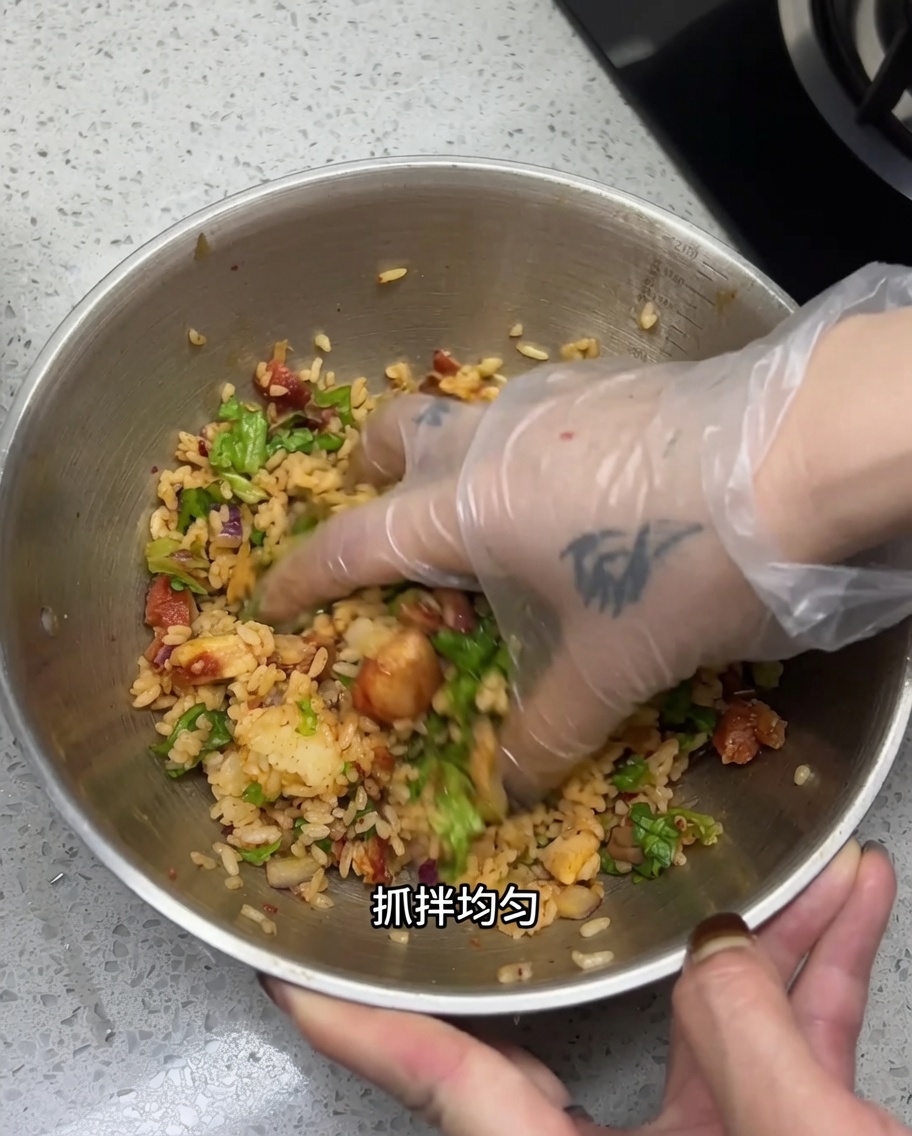 手袋をした手で、ボウルの中のご飯とチキンをしっかりと混ぜ合わせている様子。