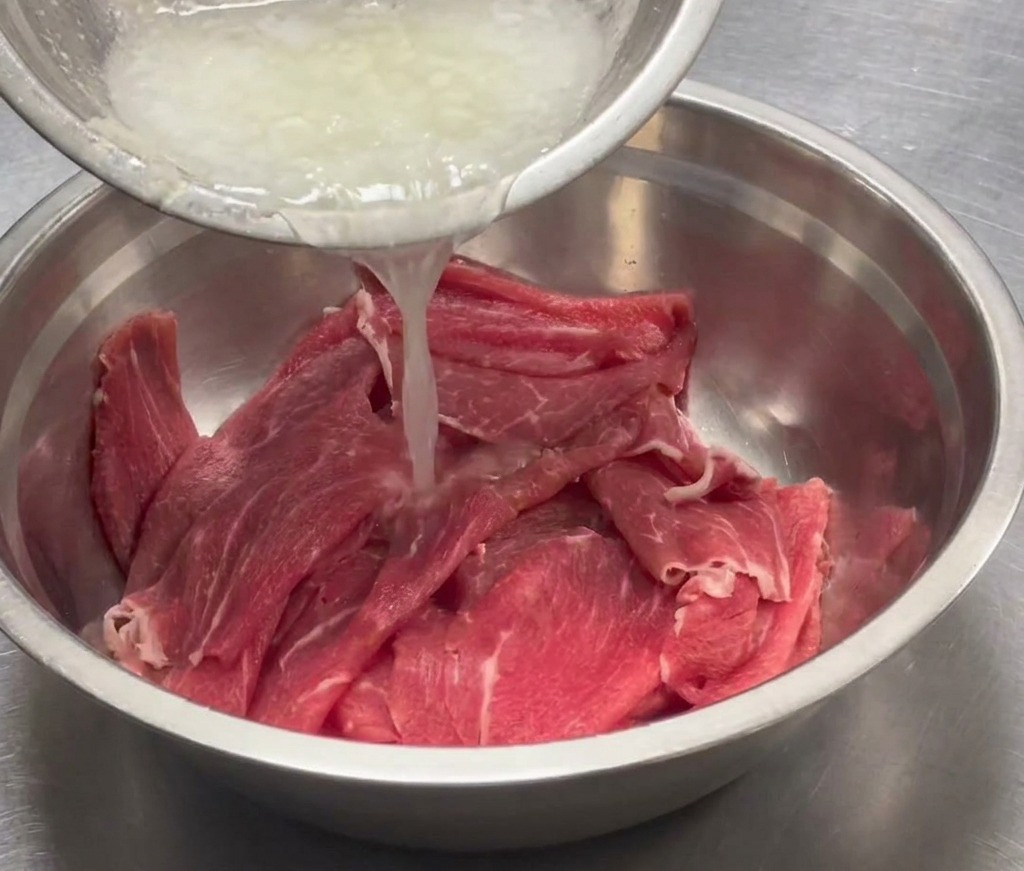 スライスした牛肉が入った大きなステンレスボウルに、ピューレを注ぎ入れている様子。