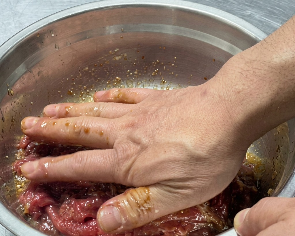 ボウルの中で生の牛肉とマリネ液を手でしっかりと混ぜ合わせている様子。