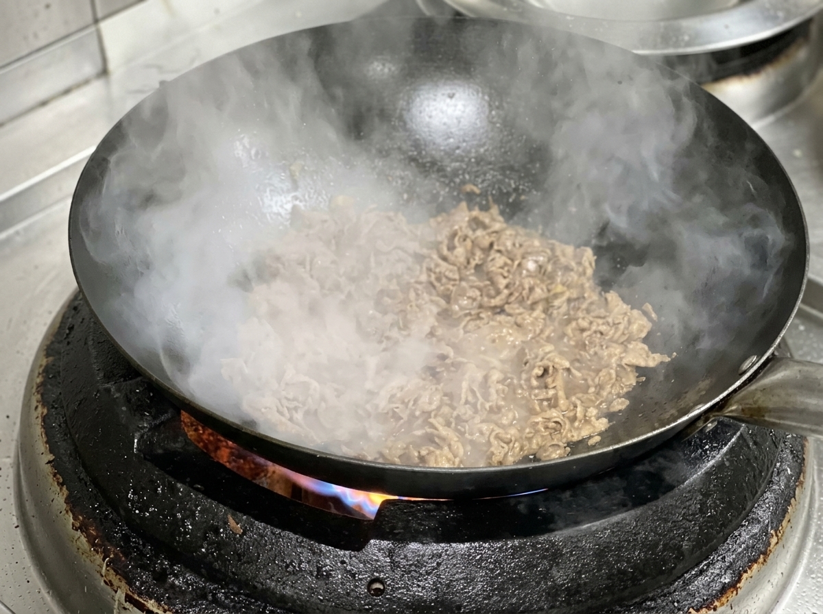 熱した中華鍋で、牛肉と玉ねぎのスライスを一緒に炒めている様子。