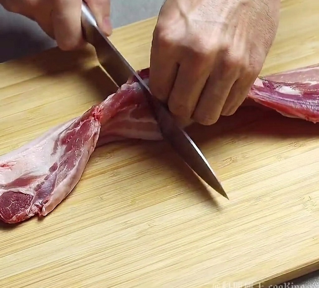 まな板の上でシェフナイフを使って豚バラ肉を厚切りにしている様子。