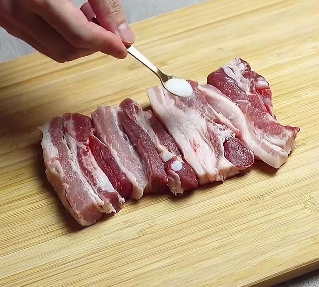 まな板に並べた豚バラ肉に塩を振っている様子。