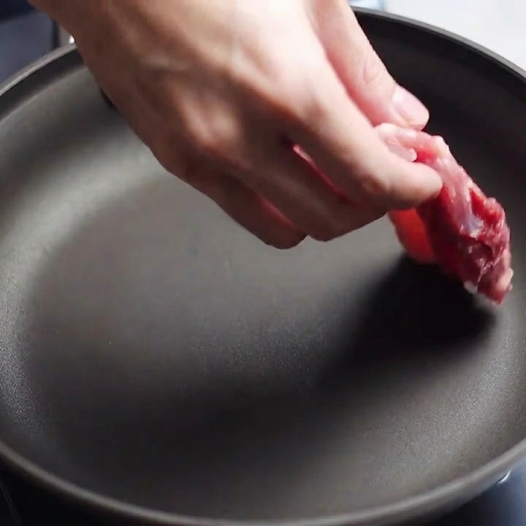 熱したフライパンに下味をつけた豚バラ肉を並べている様子。