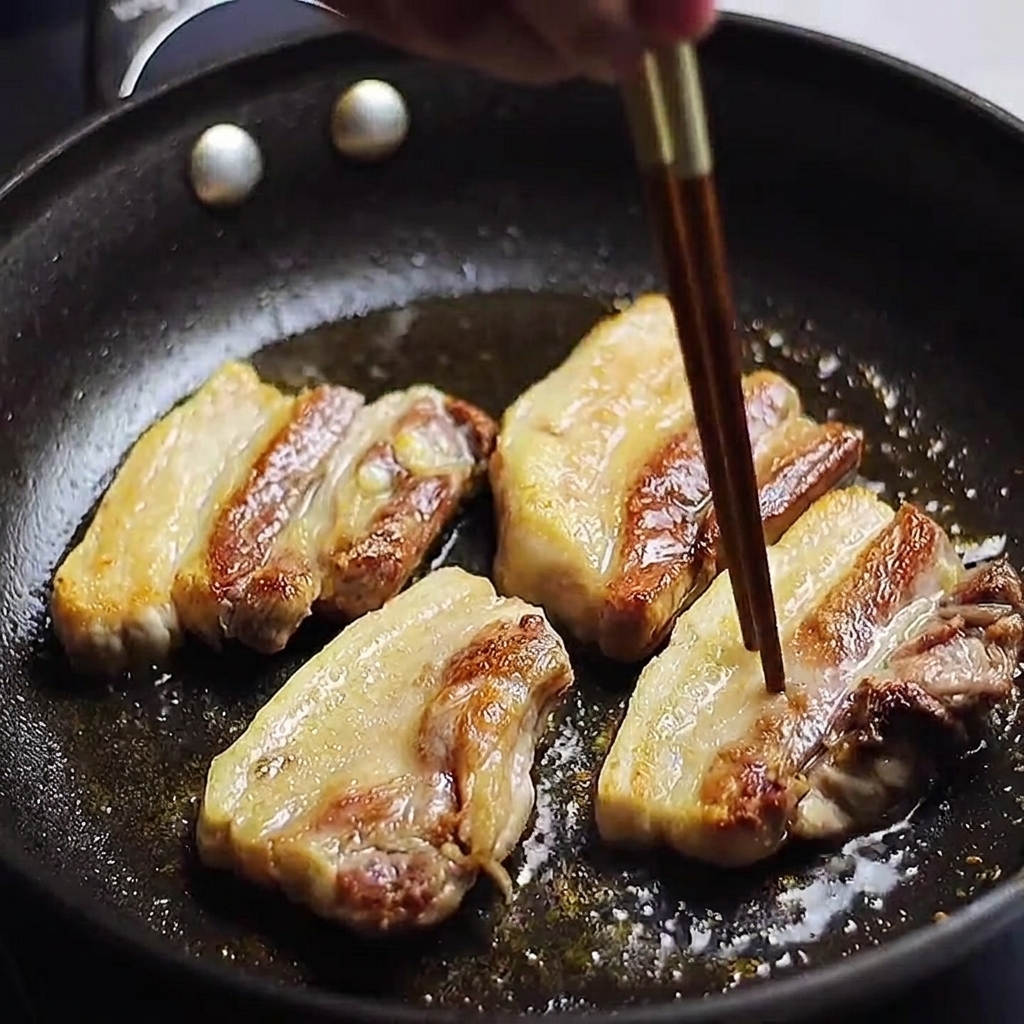フライパンで焼いている豚バラ肉に箸を刺して火の通りを確認している様子。