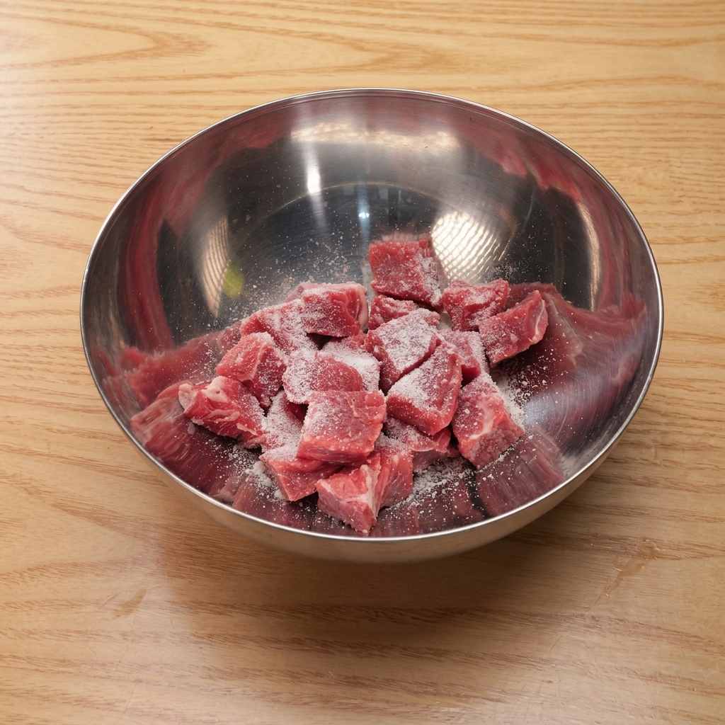 金属ボウルで牛肉を塩、砂糖、醤油、片栗粉と和えている様子。