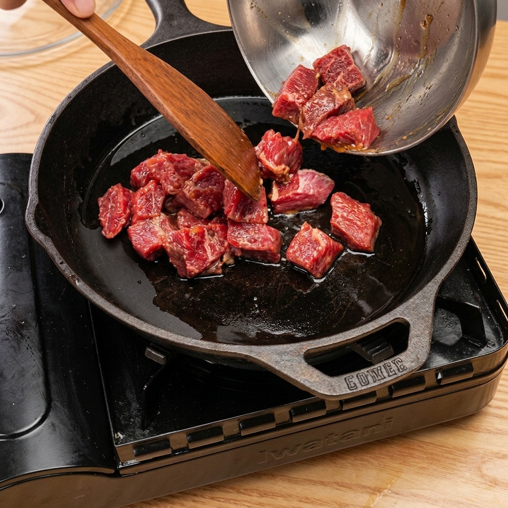 熱した鋳物フライパンで牛肉を焼いている様子。料理酒を加えて蓋をしている。
