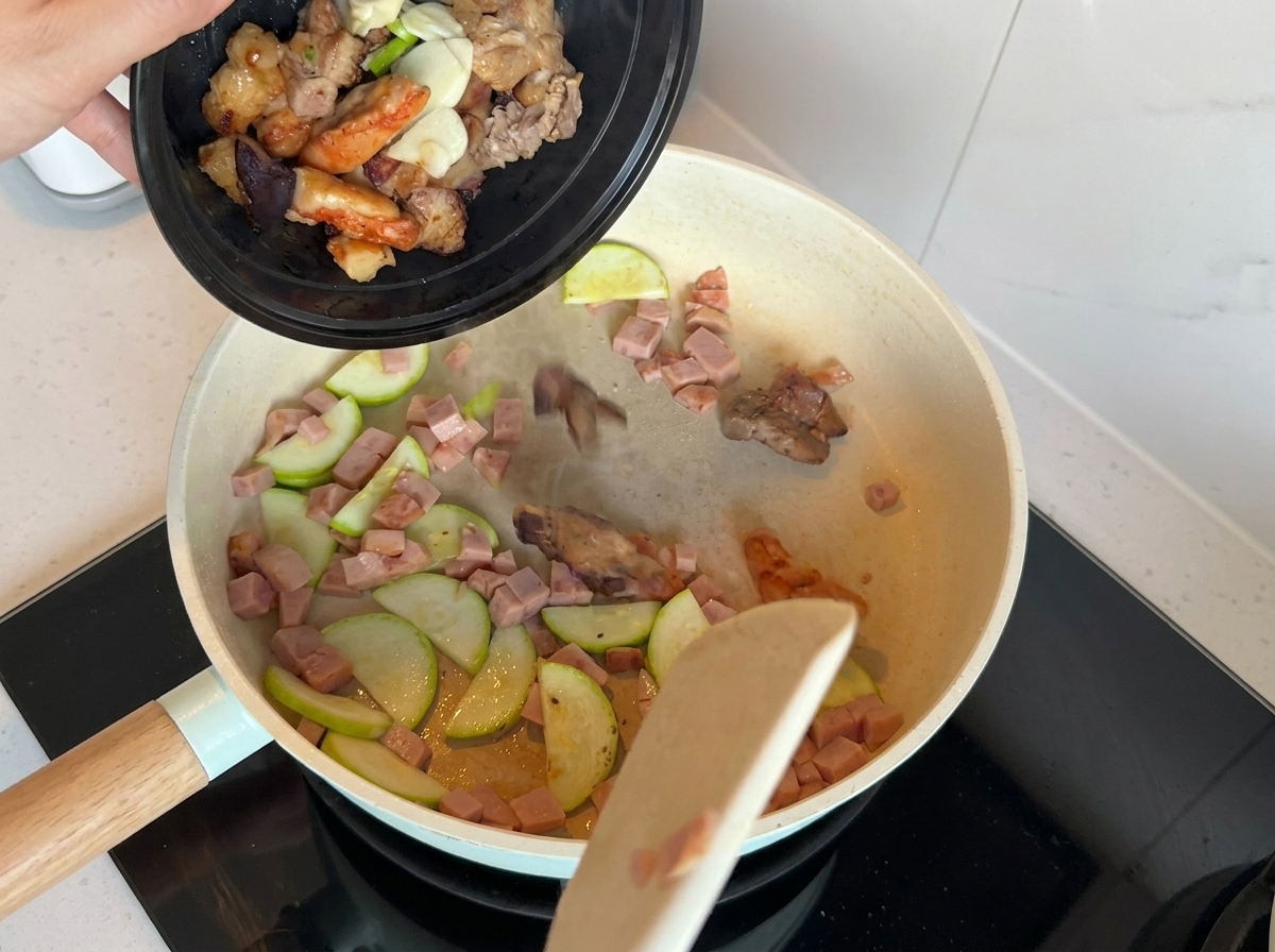炒めたズッキーニとランチミートに、刻んだ長ねぎ、にんにく、肉を追加したフライパン。