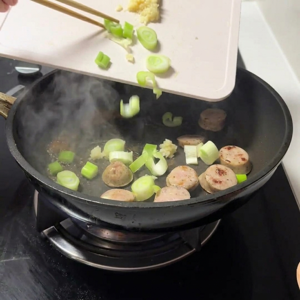 刻んだ青ねぎとみじん切りにしたにんにくを、お肉の入ったフライパンに入れている様子。