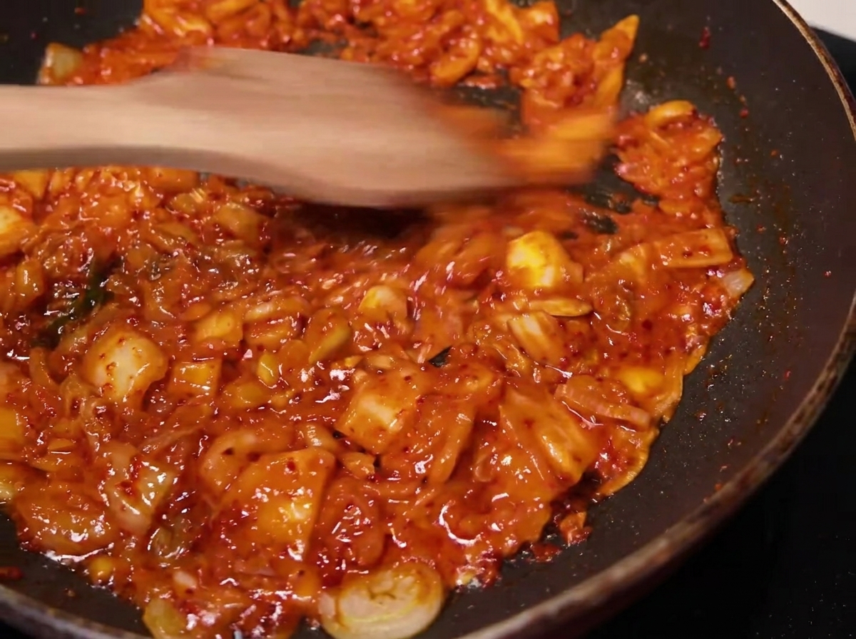 木製のヘラを使って、味付けしたキムチをフライパンで炒めている様子。