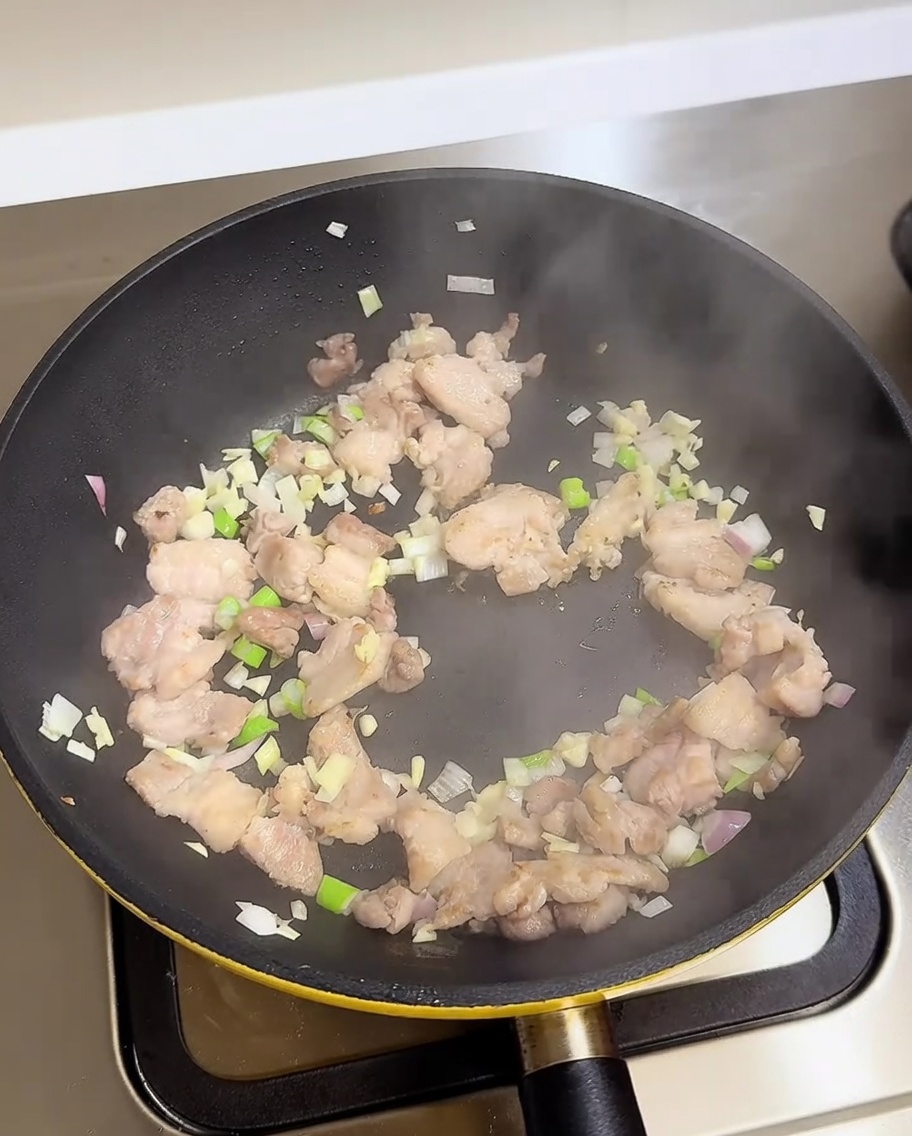 調味料を加え、豚肉、青ねぎ、にんにく、玉ねぎをフライパンで炒め合わせる様子。