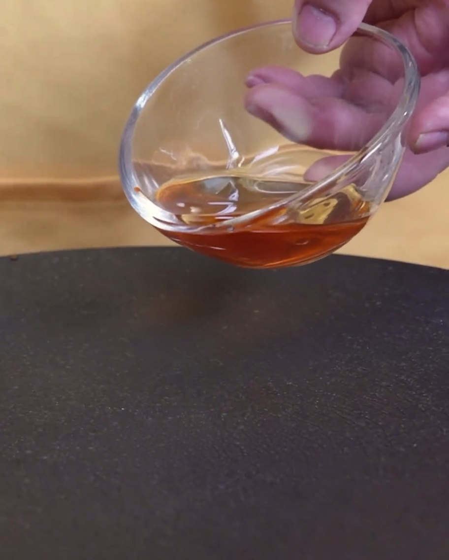 ガラスのボウルから熱したフライパンにごま油を注いでいる様子。