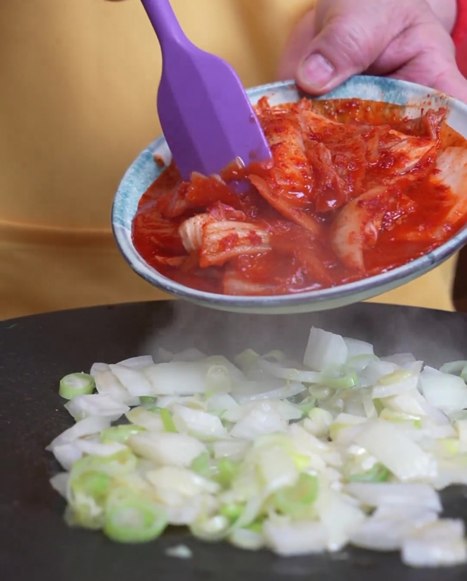 炒めた青ねぎの中にキムチを加えている様子。