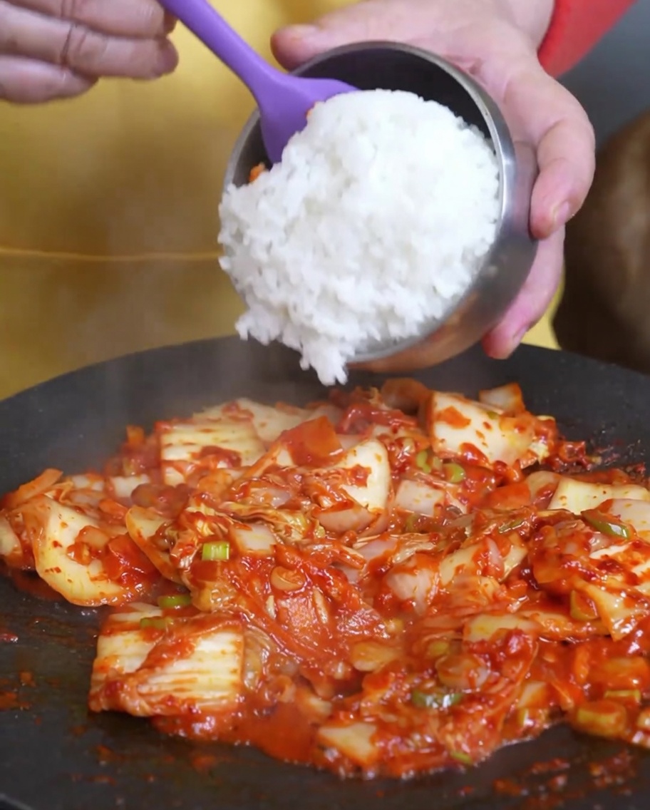 炒めたキムチの入ったフライパンにご飯を加えている様子。
