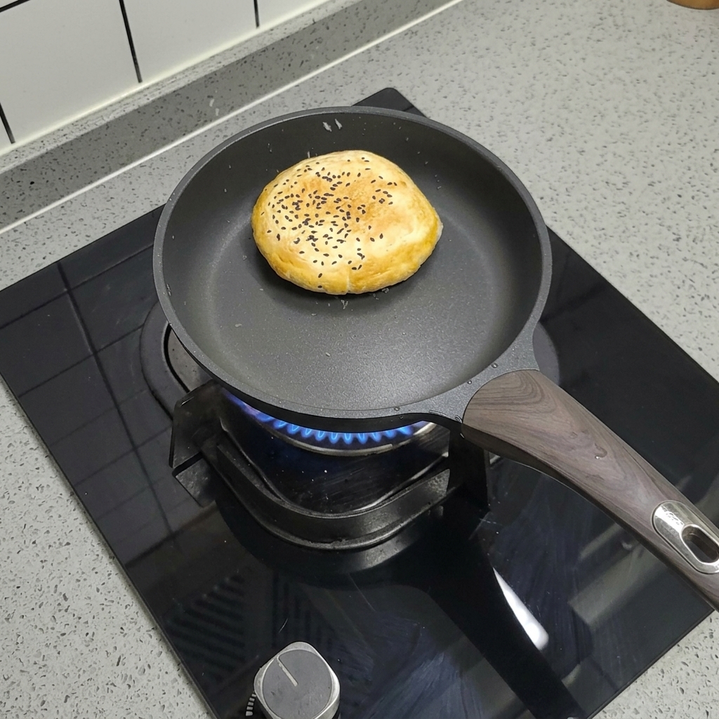 ノンスティックフライパンで焼かれるゴマ付きの冷凍バーガーバンズ