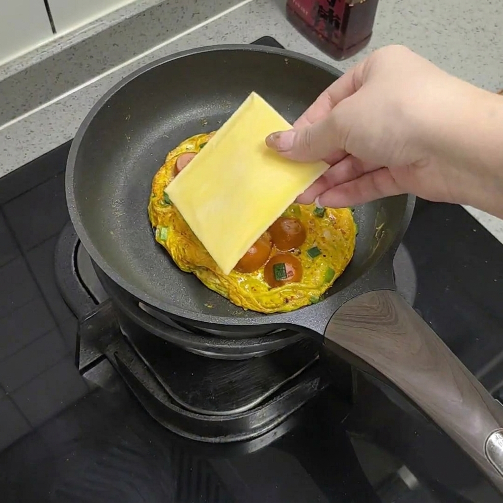 卵とソーセージの上にチーズをのせて溶かす様子