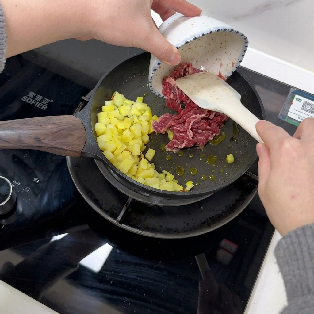 フライパンの中のじゃがいもに、生の牛肉スライスを加えている様子。