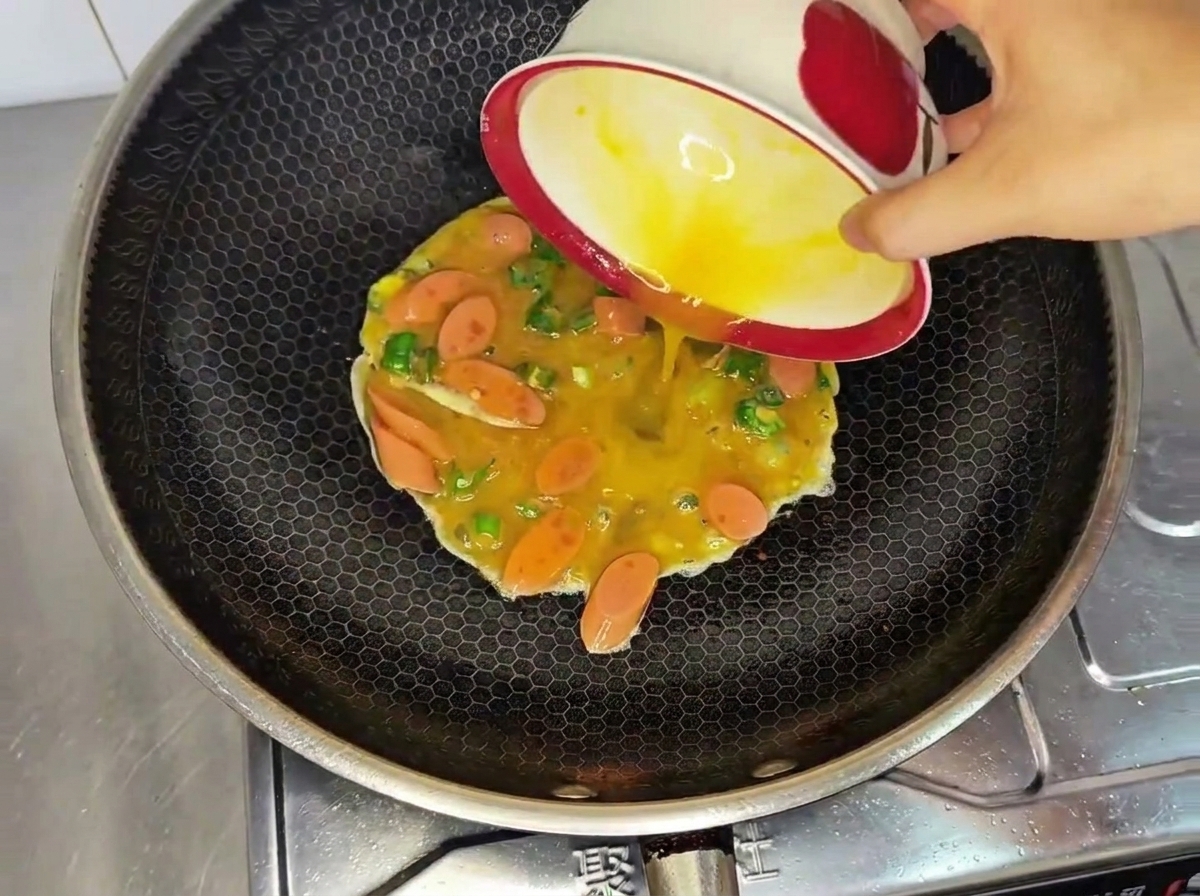 チキンパティを揚げた後の油が残る鍋に、卵液を注ぎ入れている様子。