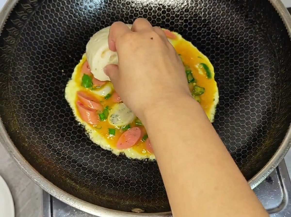 固まりかけの卵液の上に、バンズを押し付けている様子。