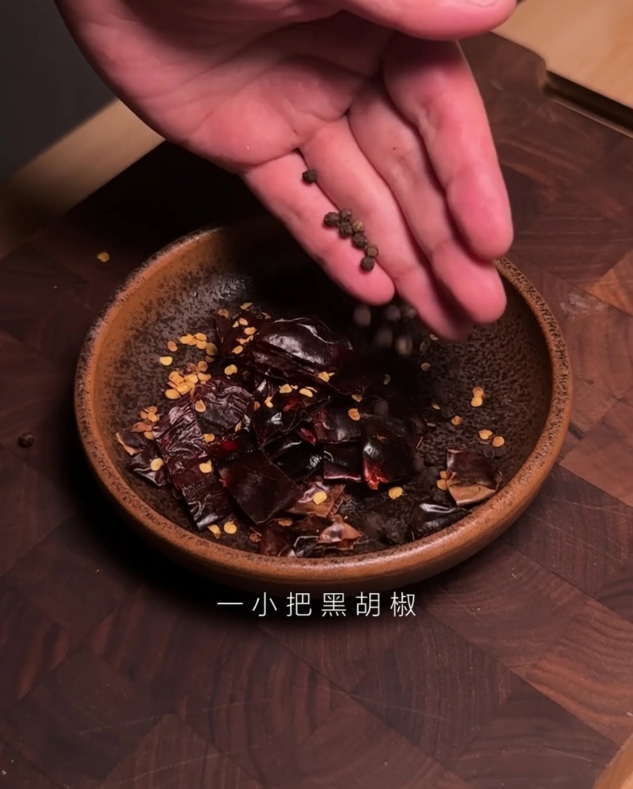 刻んだ乾燥グアヒージョチリが入ったボウルに、黒粒こしょうを加えている様子。