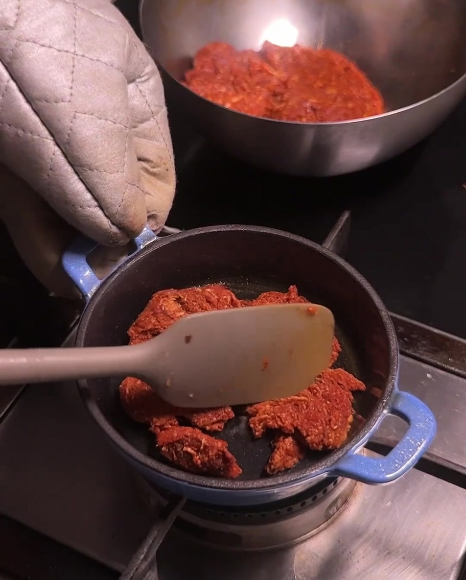 コンロの上の青い小鍋で、ほぐされた豚肉のチョリソーをスパチュラで炒めている様子。