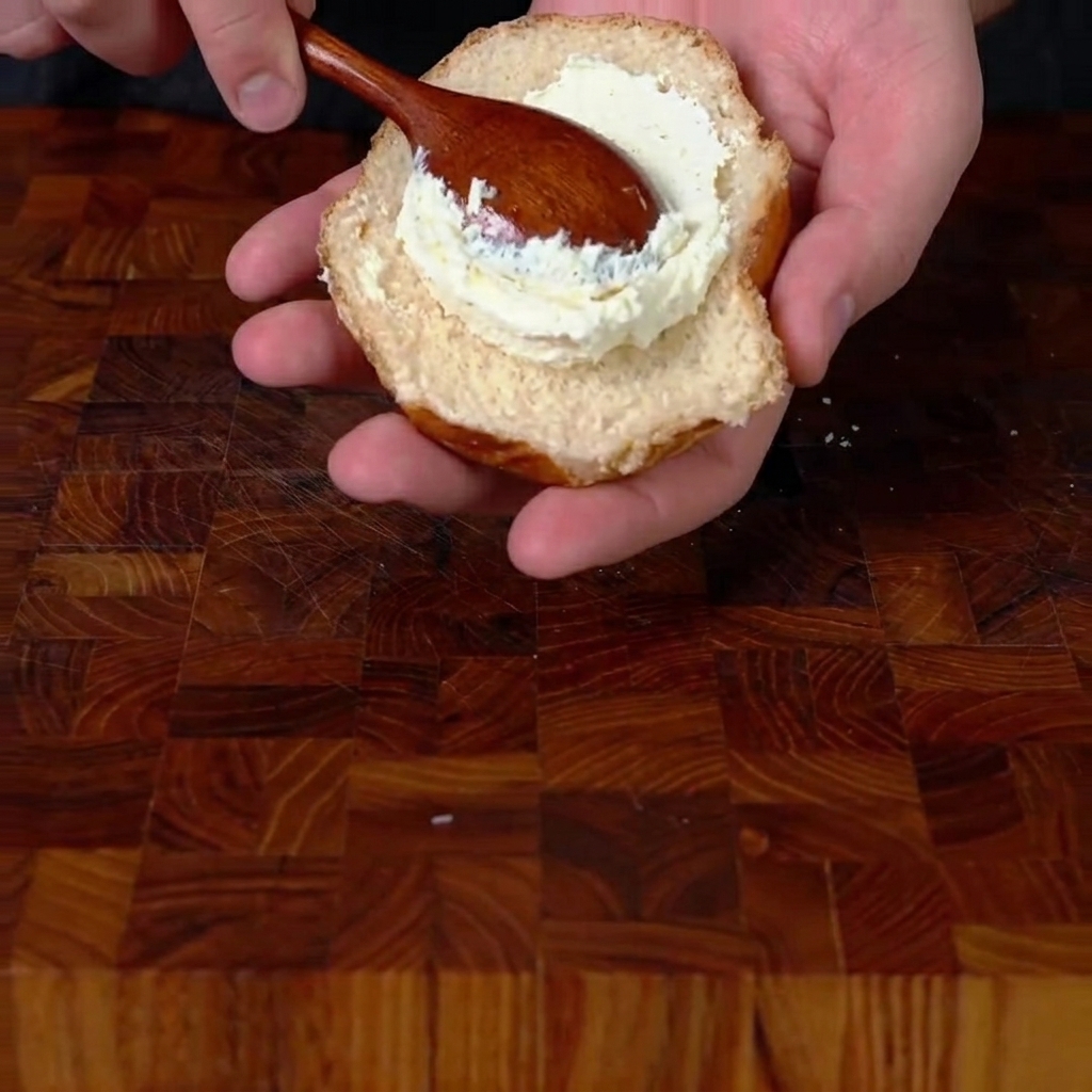 軽くトーストしたバンズの下半分に、ホイップクリームチーズをたっぷりと塗っている様子