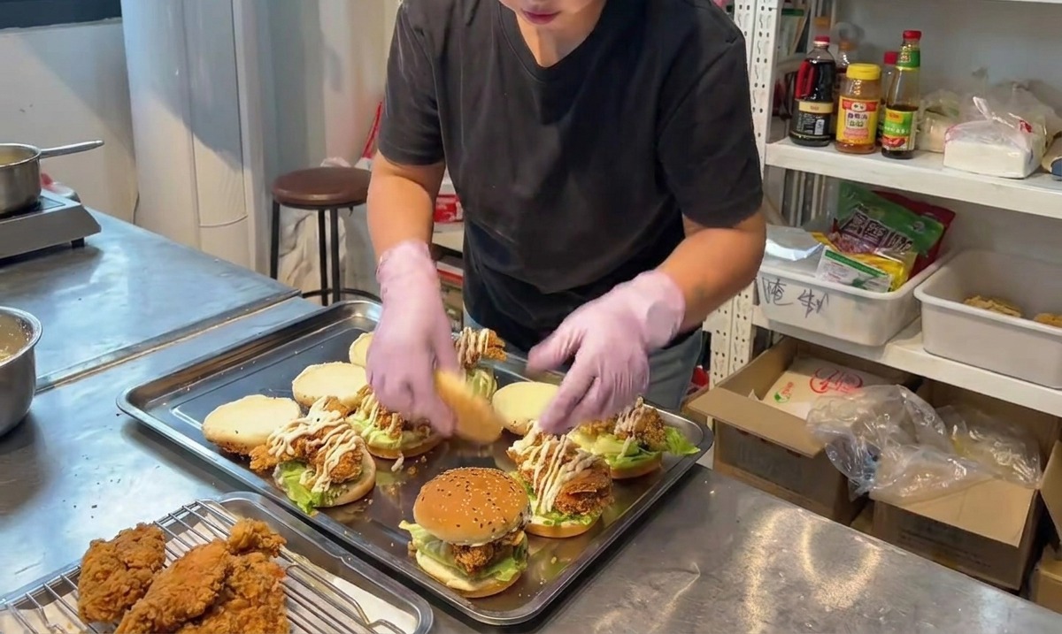 組み立てたフライドチキンバーガーの上に、ごま付きバンズの上半分を乗せている様子。